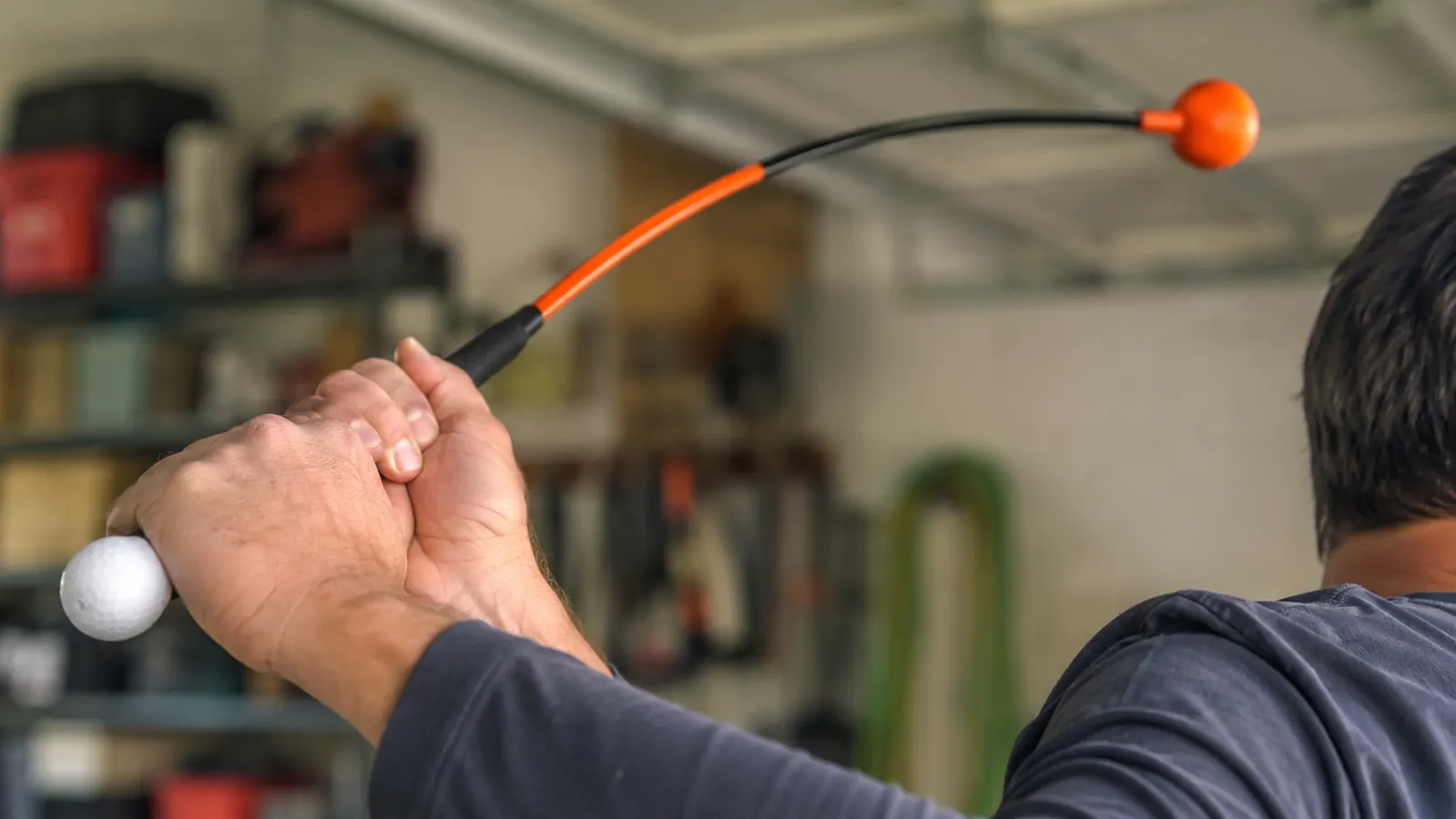 Close-up of hands gripping the orange-shafted swing trainer at the top of a slow, controlled backswing