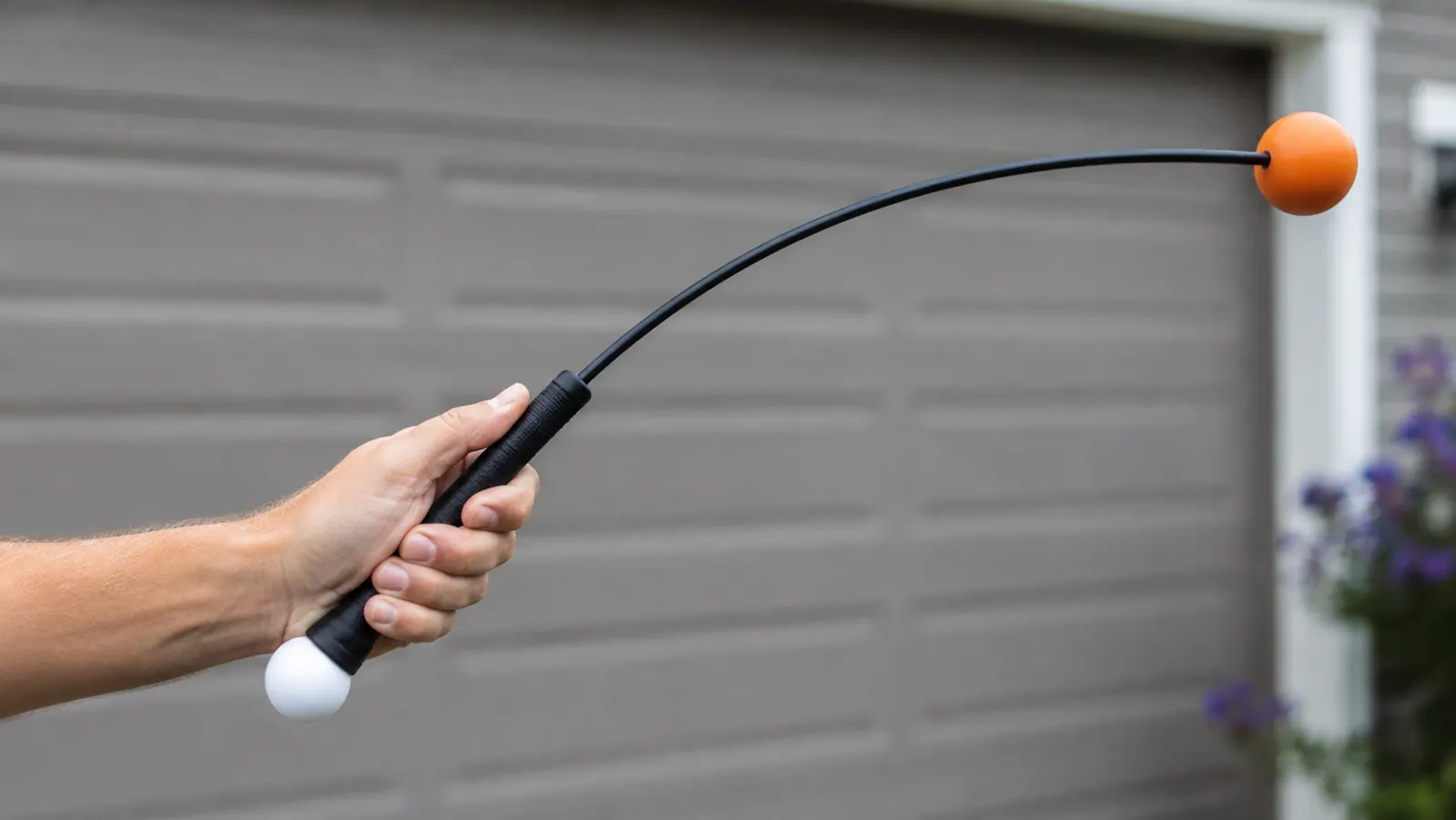 Close-up of a hand gripping the Orange Whip trainer's handle mid-swing with the flexible shaft curved from the weighted orange ball