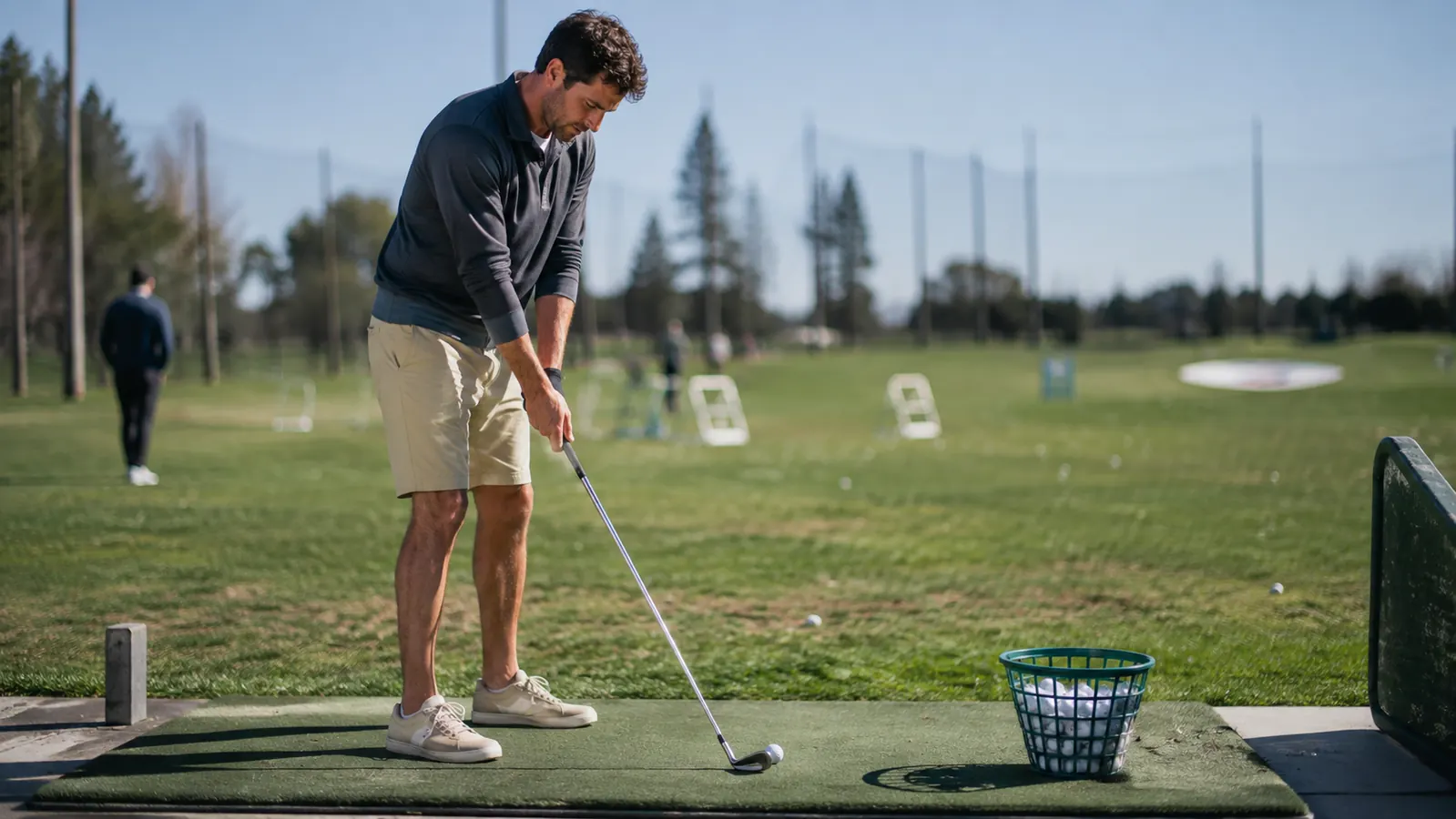 Golfer setting up over a ball on a driving range mat with a bucket of balls nearby