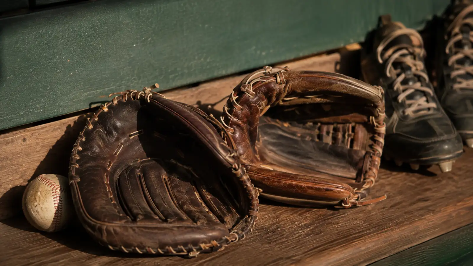 Two premium leather infield gloves, a Wilson A2000 and a Rawlings Heart of the Hide, laid side by side on a dugout bench